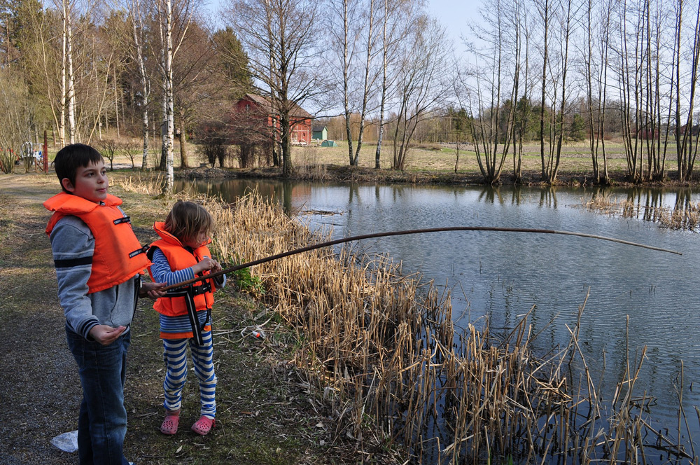 two kids in life jackets fishing on river bank