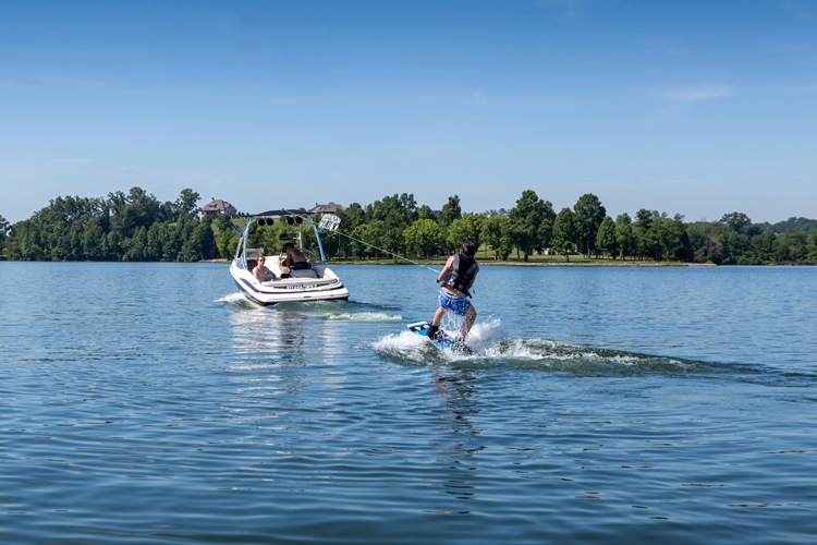 guy wakeboarding behind an inboard motor boat with a wakeboard tower